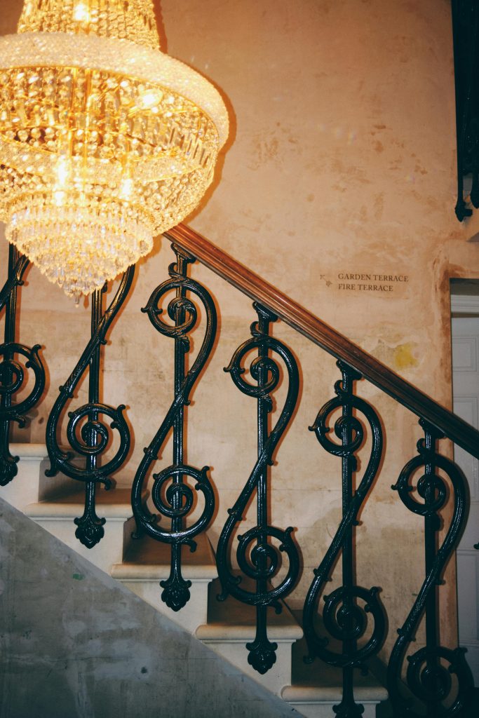 pexels-photo-29251113-29251113 Luxurious chandelier illuminating vintage staircase with ornate iron railing.